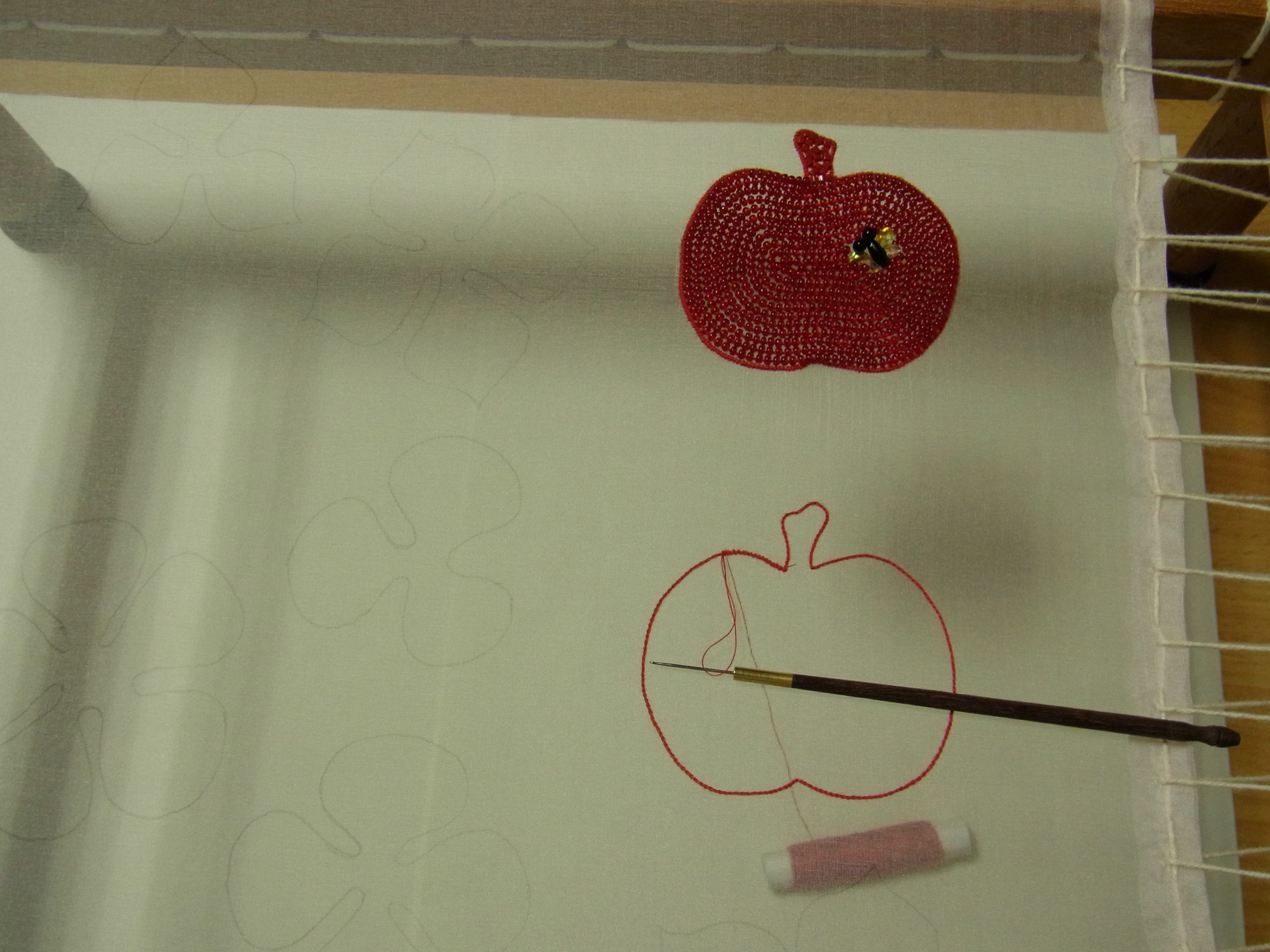 アリワークで、リンゴを赤のビーズで刺し右上に蜂を刺しています。