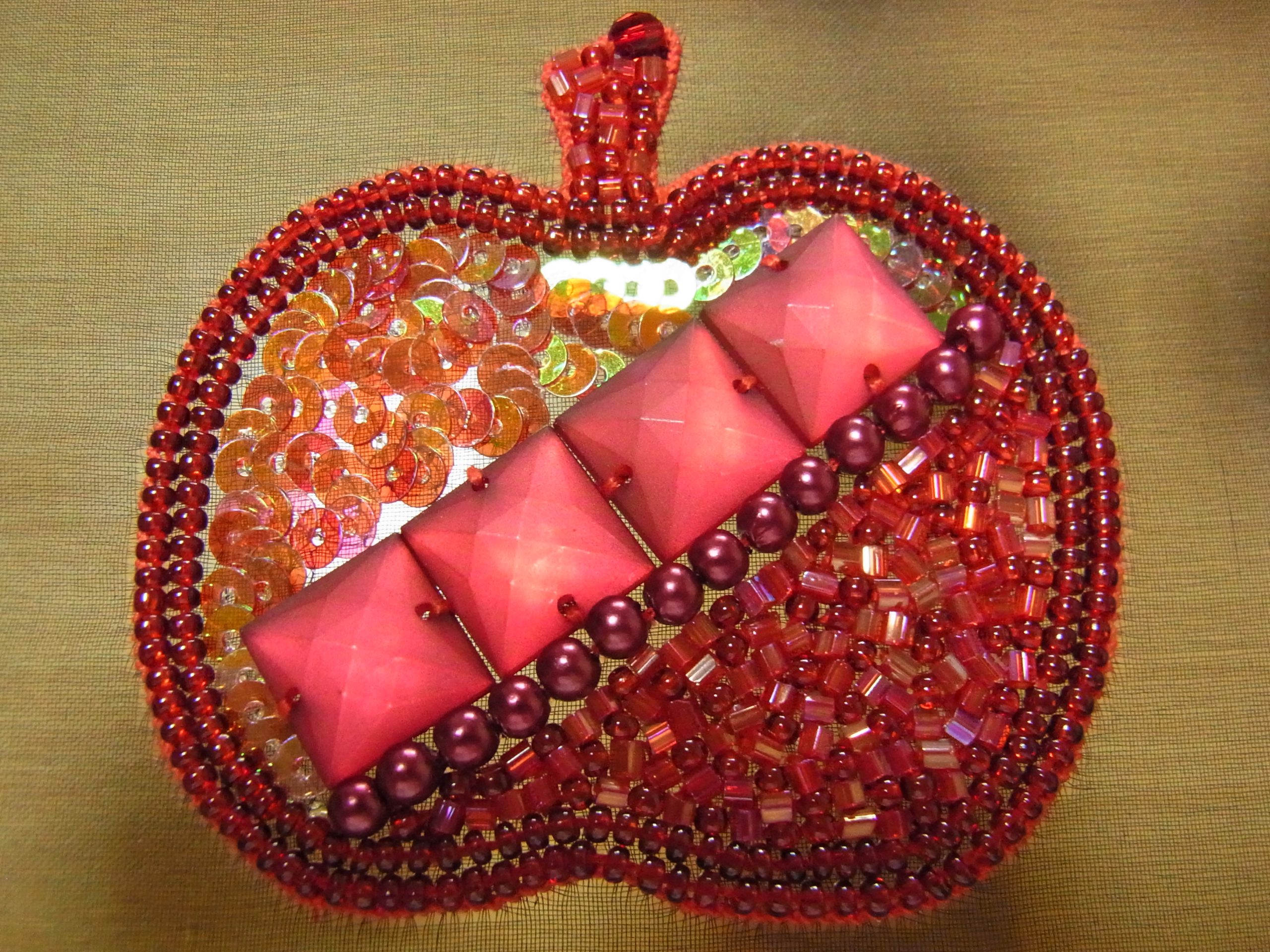赤いリンゴの中央に、スクエア型のスパンコールが4個刺してあります。両端には、メタルボール、スパンコール、丸小ビーズが刺してあります。