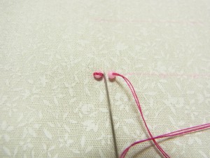 前のビーズを止めている糸の横に針を落とし、糸が一列に並ぶように刺します。