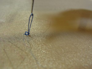 図案線上を刺しています。片方の手で糸を掛け、もう一方の手で針を180°回転させながら、針を引き揚げます。
